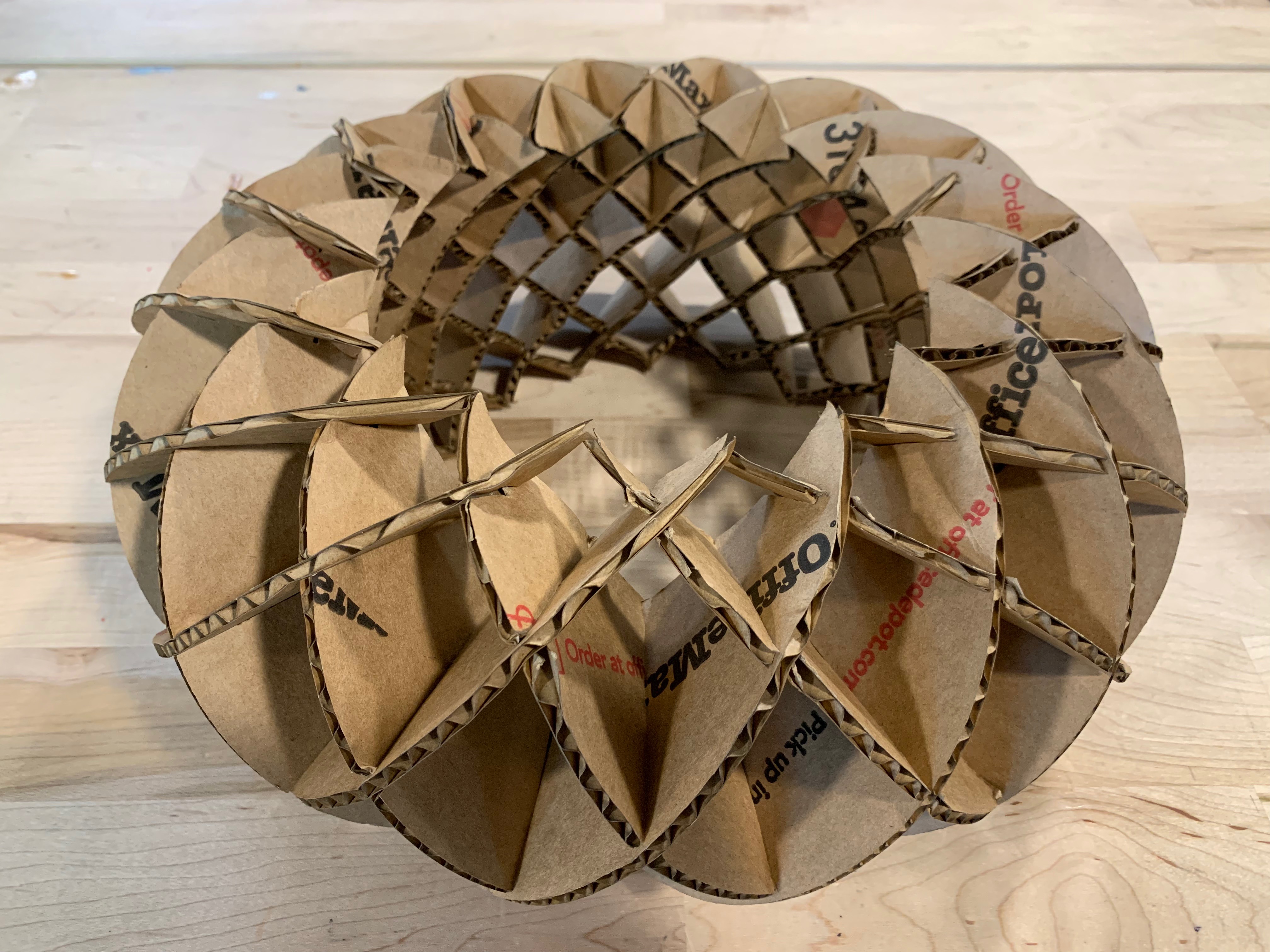 a round sculpture made of brown cardboard pieces laser cut into moon shapes with slots in them.