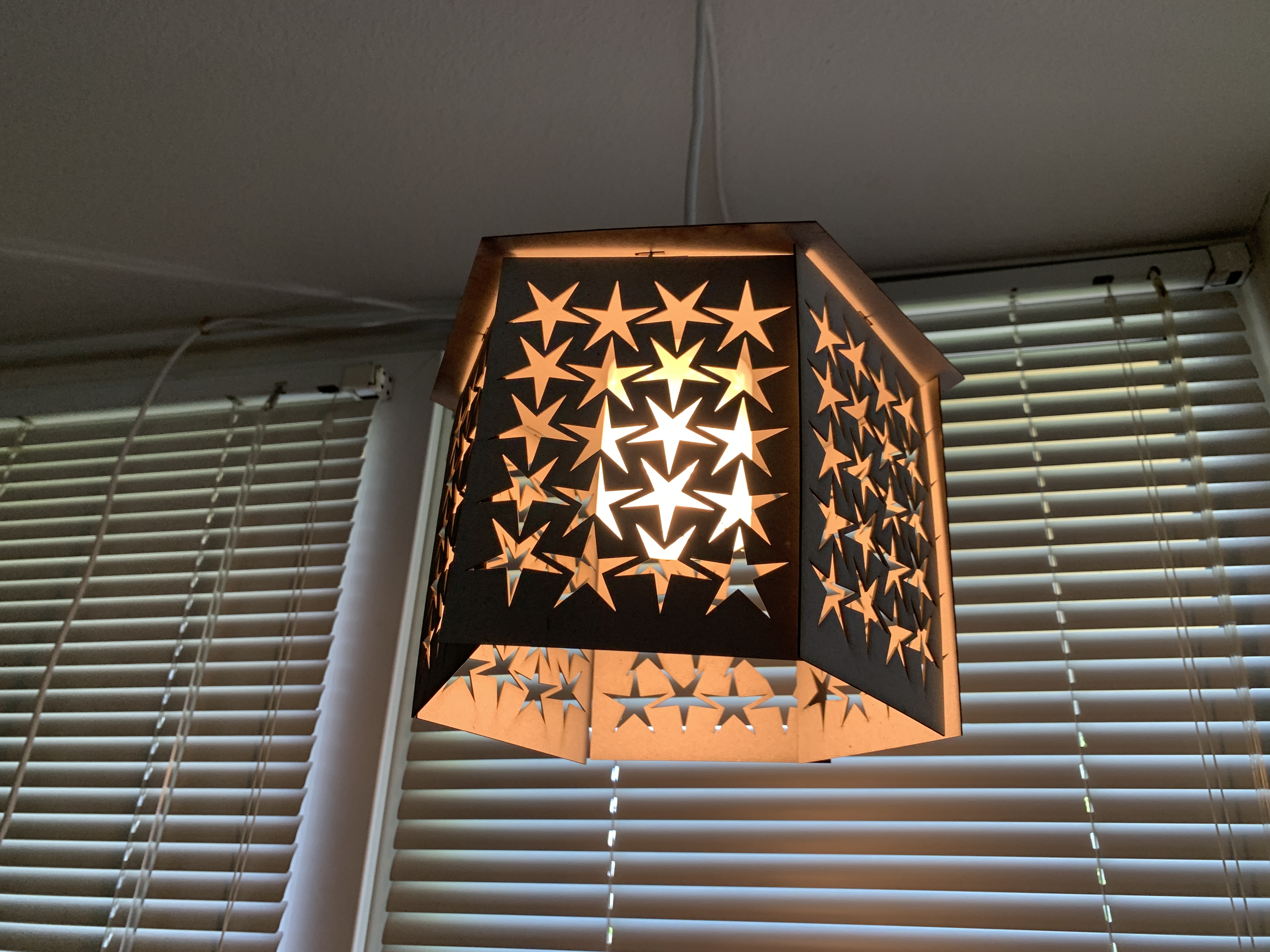 a pendant lamp made of a laser cut plywood hexagon and 3D printed cylinder, with star shapes cut out of the pieces.